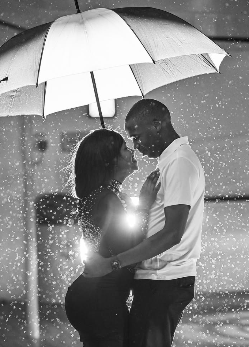 Black and white backlit photograph of a couple sharing an umbrella in heavy rain